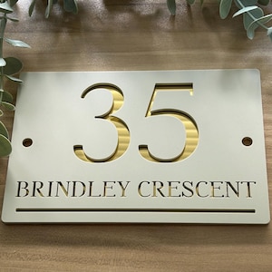 Op de afbeelding: Een rechthoekig huisnummerbord met het nummer "35" uitgesneden, waardoor een goudkleurig interieur zichtbaar wordt. Het bord toont ook de straatnaam "BRINDLEY CRESCENT". Twee kleine gaten bevinden zich aan weerszijden.