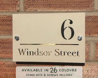 May include: A beige house number sign with the number "6" and the text "Windsor Street" in gold lettering. The sign has two silver screws on the top and bottom.