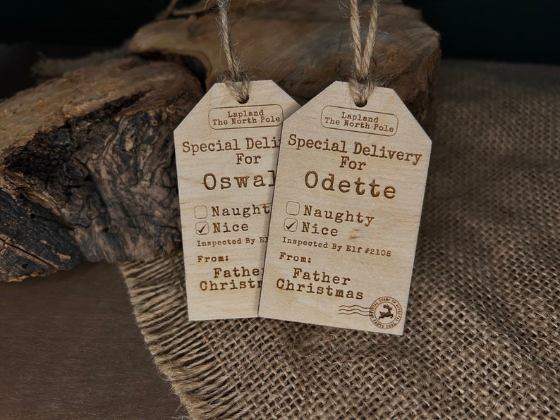 May include: Two wooden Christmas gift tags with a rustic brown finish. Each tag has a checklist for "naughty" or "nice" and a space for a name. The tags read "Special Delivery for Oswald" and "Special Delivery for Odette". Both tags are labelled "Lapland The North Pole" and "From: Father Christmas".