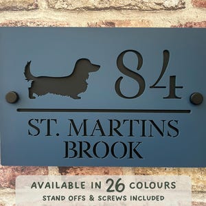 Può includere: Un cartello blu per il numero civico con una silhouette di bassotto nera, il numero 84 e il testo "ST. MARTINS BROOK".