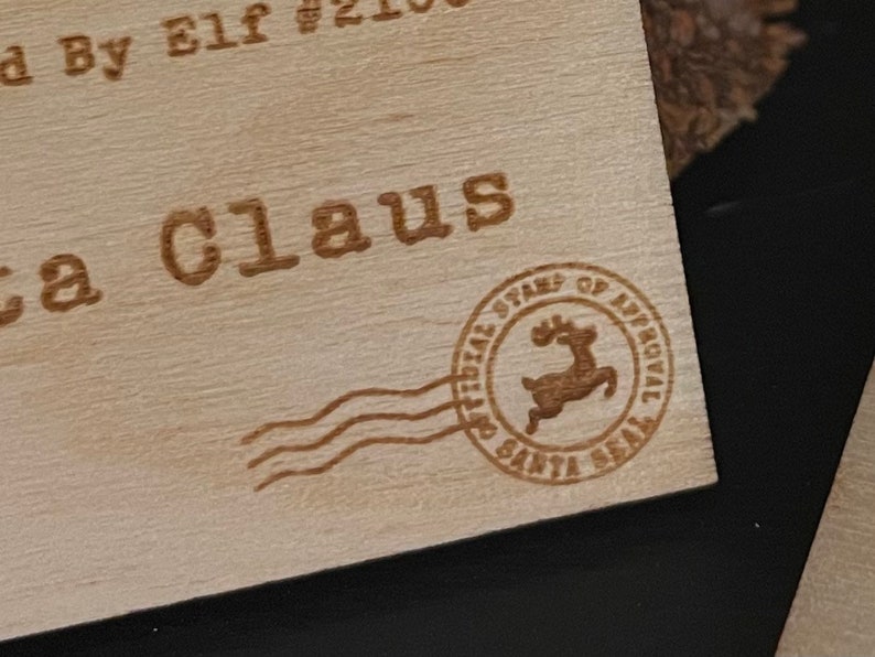May include: A wooden tag with the text "Santa Claus" and a red reindeer stamp with the text "Official Stamps of Approval Santa Seal".