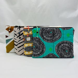 Peut inclure: Quatre pochettes zippées rectangulaires en tissu disposées en rangée. La pochette avant est turquoise avec des motifs de lignes circulaires noires. Les autres présentent des imprimés géométriques, rayés et pointillés, avec des tirettes perlées.