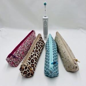 Peut inclure: Quatre trousses en tissu à motifs, dont des motifs floraux et léopard, sont présentées avec une brosse à dents électrique grise. Chaque trousse a une fermeture éclair et est conçue pour contenir une brosse à dents.