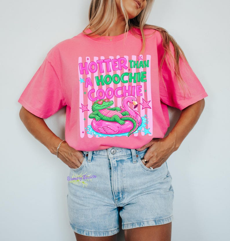 Puede incluir: Camiseta rosa brillante con la frase "Hotter Than A Hoochie Coochie" en verde y rosa. El gr&aacute;fico muestra un caim&aacute;n verde con gafas de sol en un flotador de flamenco rosa. Estilo casual.