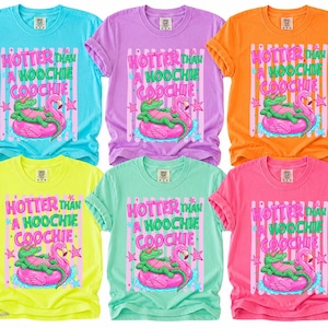 Puede incluir: Seis camisetas coloridas con la frase "HOTTER THAN A HOOCHIE COOCHIE". El dise&ntilde;o muestra un caim&aacute;n verde sobre un flamenco rosa. Las camisetas est&aacute;n disponibles en azul, morado, naranja, amarillo, verde y rosa.