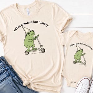 Peut inclure: Ensemble t-shirt et body crème. Le t-shirt présente une grenouille verte sur un scooter avec le texte "Off to commit dad foolery". Le body a un design similaire avec le texte "Off to commit mini foolery".