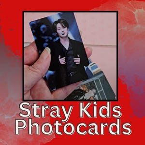 May include: A close-up of a Stray Kids photocard featuring a member of the group in a black shirt and a dark background. The photocard is being held in a hand.