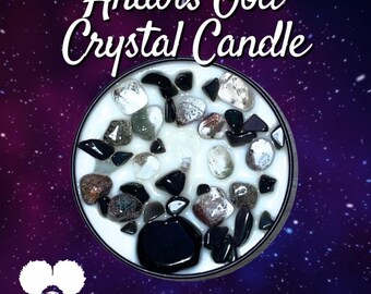 May include: A white candle with black and grey crystals embedded in the wax. The candle is in a round glass jar with a black rim. The text "Anubis God Crystal Candle" is written in black on a purple background with white stars.