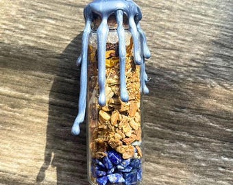 Könnte beinhalten: Eine kleine Glasflasche gefüllt mit getrockneten Kräutern, Kristallen und einem blauen Wachssiegel. Die Flasche ist mit einer Vielzahl von Kräutern und Kristallen gefüllt, darunter blaue Steine, und mit einem blauen Wachssiegel versiegelt.
