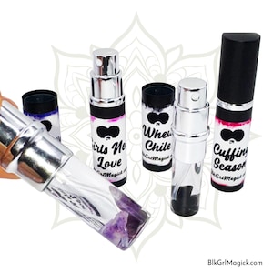 May include: A collection of perfume spray bottles with silver tops and black caps. The bottles have labels with phrases like "Girls Need Love" and "Cuffing Season." One bottle is filled with purple crystals.