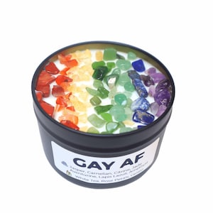 Może przedstawiać: Czarny pojemnik na świecę z napisem "GAY AF" i tęczą małych kamieni szlachetnych osadzonych w wosku. Świeca pachnie białą herbatą, płatkami róż i lodami.