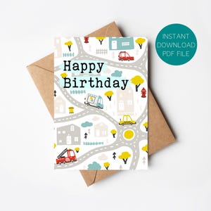 May include: A birthday card with a city scene design featuring roads, houses, and vehicles. The card has the words "Happy Birthday" in large letters. The card is on top of a brown envelope, with a green circle that says "Instant Download PDF File".