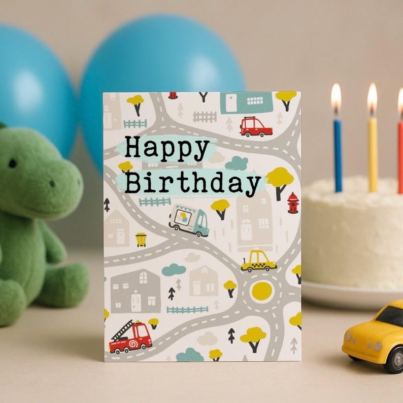 Może przedstawiać: Kartka urodzinowa z motywem mapy drogowej i napisem "Happy Birthday". Karta zawiera ilustracje samochod&oacute;w, drzew i dom&oacute;w. Na zdjęciu znajduje się r&oacute;wnież zabawkowy samoch&oacute;d i tort ze świeczkami.