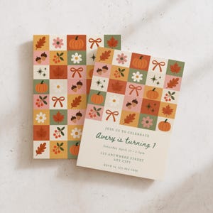 May include: A rectangular birthday invitation card featuring a grid pattern of autumn-themed icons including pumpkins, leaves, acorns, flowers, and bows in muted tones. The text reads: JOIN US TO CELEBRATE Avery is turning 1 Saturday April 15 2-5pm 123 ANYWHERE STREET ANY CITY RSVP to 123-456-7890.