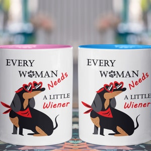 May include: Two white ceramic mugs with pink and blue rims. Each mug features a black dachshund wearing red heart-shaped sunglasses and a red bandana. The text on the mugs reads "Every Woman Needs A Little Wiener".