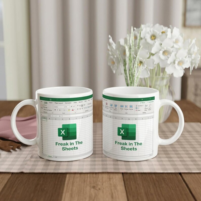 May include: Two white ceramic mugs featuring a printed graphic of a Microsoft Excel spreadsheet interface. The design includes the green Excel logo and the black text "Freak in The Sheets" centered on the front of each mug with a handle.
