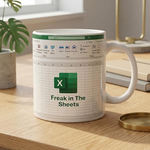Könnte beinhalten: Ein weißer Keramikbecher mit einem aufgedruckten Tabellenkalkulations-Interface, dem Microsoft Excel-Logo und dem Text "Freak in The Sheets" in Dunkelgrün. Das Design zeigt ein oberes Menüband mit verschiedenen Symbolen und ein Raster.