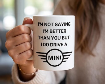 May include: A white ceramic mug featuring black text that reads I'M NOT SAYING I'M BETTER THAN YOU BUT I DO DRIVE A MINI, accompanied by a black graphic of the MINI car brand logo with wings extending from a central circle containing the word MINI.