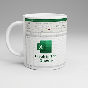 May include: A white ceramic mug featuring a printed graphic of a spreadsheet interface. The design includes the Microsoft Excel logo and the text "Freak in The Sheets" centered on the grid. The top of the mug displays a standard software ribbon.