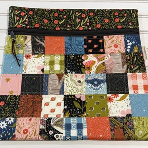 May include: A zippered pouch featuring a patchwork design of various fabric squares with floral, snail, and geometric patterns in orange, blue, green, and black. The top section is a solid black fabric with a red and green floral print.