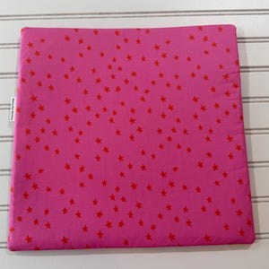 Peut inclure: Une housse de coussin carr&eacute;e en tissu rose vif, orn&eacute;e d'un motif dispers&eacute; de petites &eacute;toiles rouges pleines sur toute la surface. Une petite &eacute;tiquette en tissu blanc avec du texte noir est fix&eacute;e sur le bord lat&eacute;ral gauche de l'article textile.