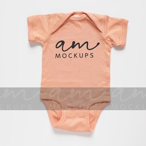 May include: A peach-coloured baby onesie with short sleeves and the text "am mockups" printed on the front.