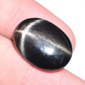 Könnte beinhalten: Ein schwarzer ovaler Cabochon-Edelstein mit einem sternförmigen Muster in der Mitte.