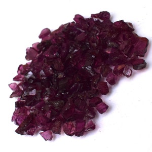 Puede incluir: Un montón de virutas de piedras preciosas de color morado oscuro. Las virutas tienen una forma irregular y un acabado brillante.