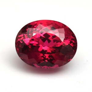 Puede incluir: Una gema facetada, de forma ovalada, en un tono rojo vibrante. La superficie de la gema refleja la luz, mostrando sus intrincados cortes y su estructura interna. La gema se encuentra sobre un fondo blanco liso, resaltando su color y claridad.