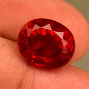 Könnte beinhalten: Ein ovaler Edelstein in tiefroter Farbe mit einem facettierten Schliff.