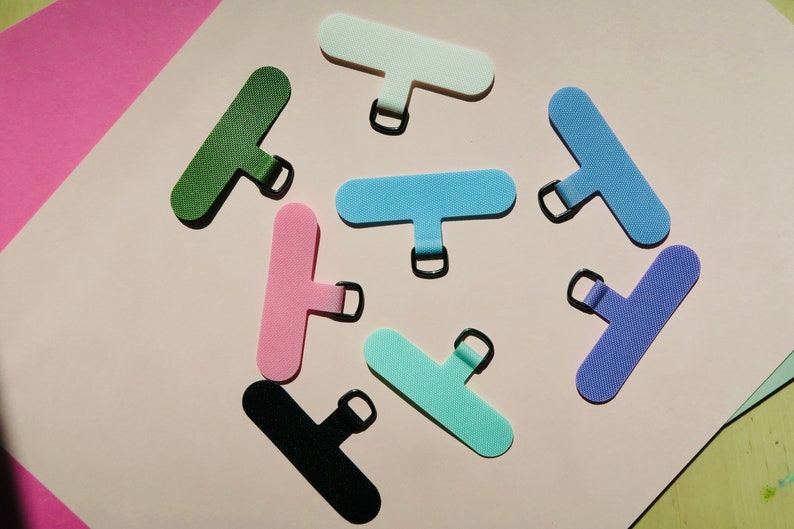 May include: Assortment of eight colorful, rectangular, fabric cable ties with a metal ring. The ties are in various colors, including green, pink, light blue, white, turquoise, and purple.