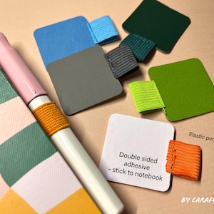 May include: Assortment of colorful felt squares with double-sided adhesive for sticking to notebooks. Each square has an elastic pen loop band attached. The text "Double sided adhesive - stick to notebook" and "Elastic pen loop band" are visible in the image.