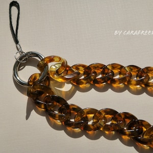 May include: A brown tortoiseshell chain phone strap with a silver ring and a black strap.