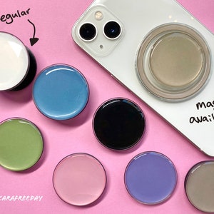 May include: Assortment of colourful phone pop sockets, including white, blue, green, pink, purple, and grey. The text "regular" is written on the image. A white phone with a grey magnetic pop socket is shown in the background. The text "magsafe available" is written on the image.