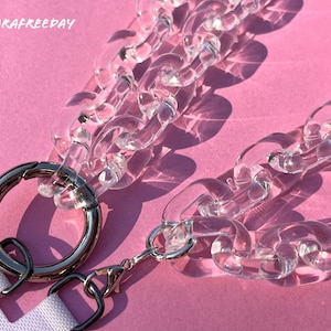 May include: A clear plastic chain with a silver ring and a silver clasp. The chain is on a pink background.