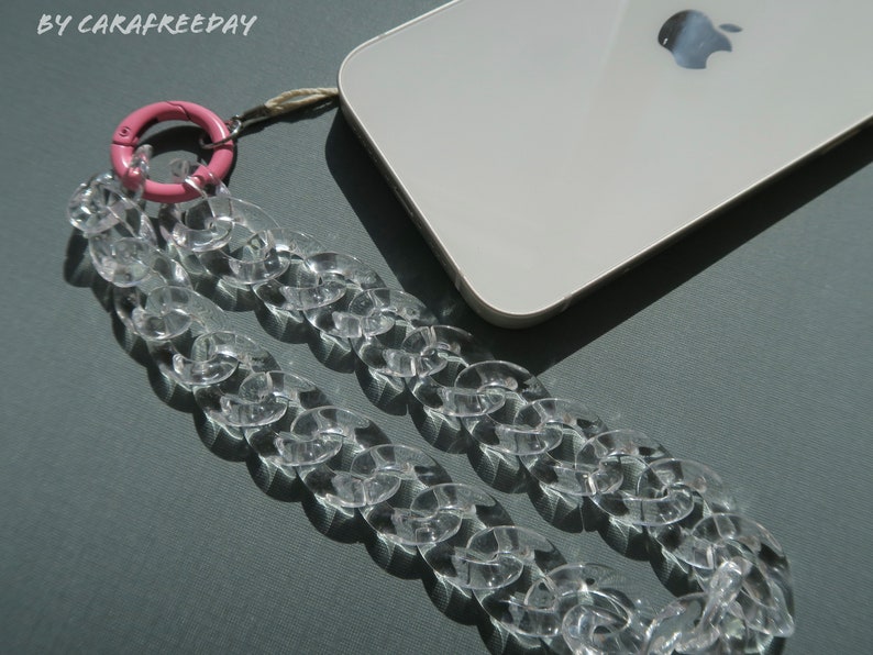 Op de afbeelding: Een transparante plastic ketting telefoonband met een roze plastic ring bevestiging. De band is ontworpen om om de nek of pols te worden gedragen.