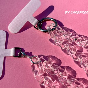 May include: Two clear acrylic chain phone straps with silver clasps and metal rings. The straps are attached to white T-shaped adhesive strips. The text "BY CARAFREEDAY" is visible in the upper right corner of the image.