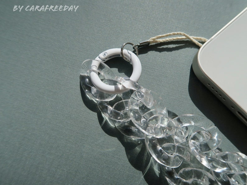 Op de afbeelding: Een transparante telefoonriem van kunststofketting met een witte metalen sluiting en een wit touwtje.
