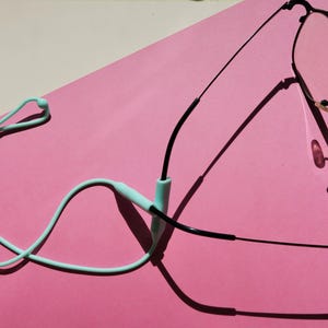 May include: A pair of black-framed eyeglasses attached to a light mint green silicone glasses strap. The strap features a sliding adjustment bead and two cylindrical connectors that secure onto the thin black temple arms of the eyewear.