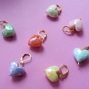 Könnte beinhalten: Sechs herzförmige Ohrringe mit goldenen Haken. Die Herzen sind aus irisierendem Keramik und in verschiedenen Pastellfarben erhältlich, darunter hellblau, hellgrün, hellrosa, Pfirsich und Gelb.