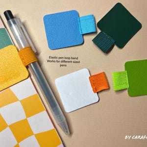 May include: A set of colorful pen loop bands made of elastic material. The bands are attached to square pieces of paper in various colors, including yellow, blue, white, green, and black. The text "Elastic pen loop band Works for different sized pens" is printed on the white paper.