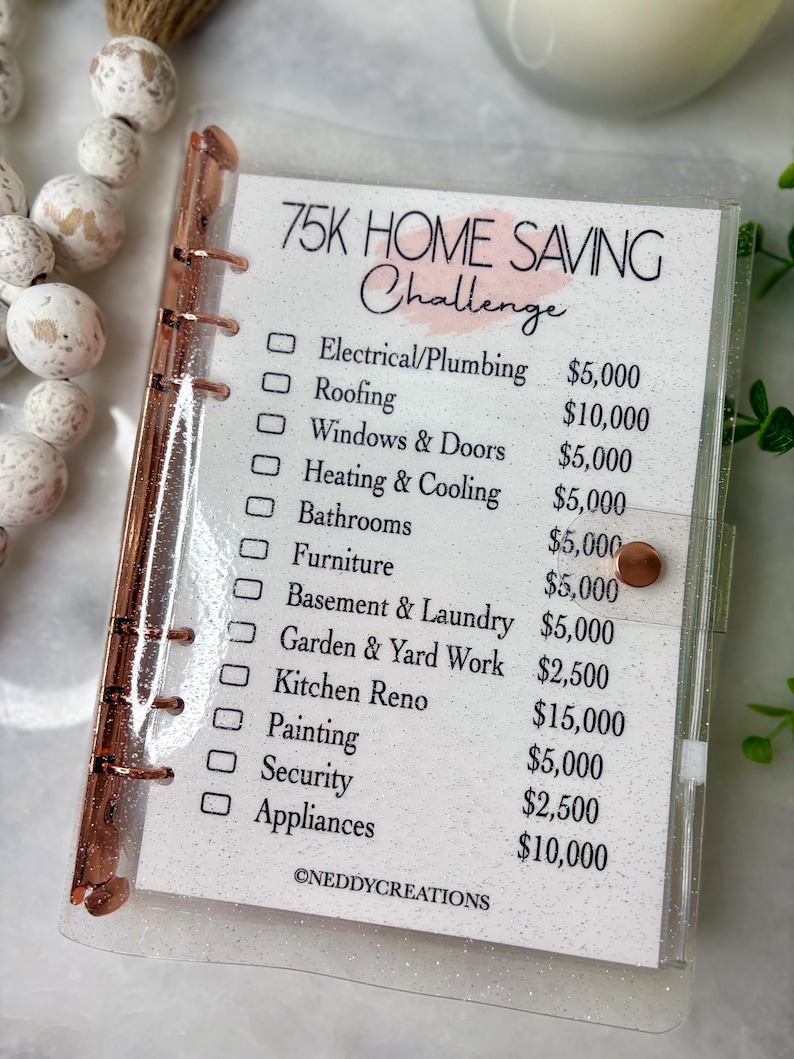 May include: A clear, glittery binder with rose gold accents holds a savings challenge checklist. The text "75K HOME SAVING Challenge" is at the top, with categories like "Roofing" and "Appliances" listed below, each with a dollar amount.