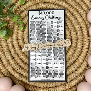 May include: A black and white savings challenge chart with a wooden sign that says "Neddy Creations LLC". The chart is divided into squares with dollar amounts ranging from $5 to $300. The chart is titled "$10,000 Savings Challenge".