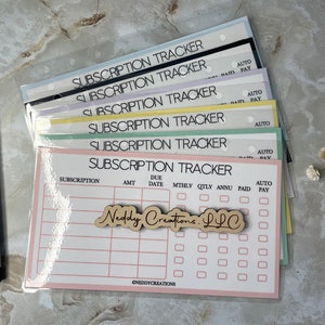 May include: A stack of pink, green, blue, yellow, and white subscription tracker sheets with a wooden sign that says "Neddy Creations LLC". The sheets have columns for subscription, amount, due date, monthly, quarterly, annually, paid, and auto pay.