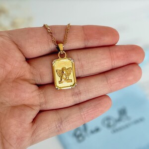 Gold angel charm necklace held in hand to show pendant size and scale against skin