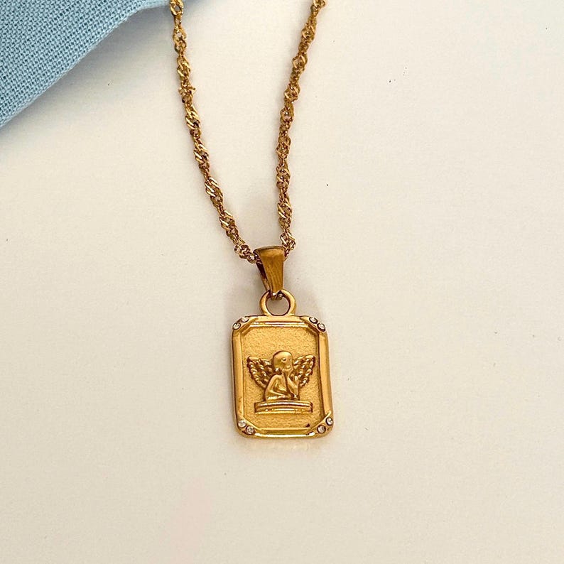 18k gold angel necklace with rectangular cherub pendant on a delicate gold chain displayed on a soft cream background