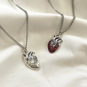 May include: Two silver necklaces with anatomical heart pendants. One heart is silver, the other is red.