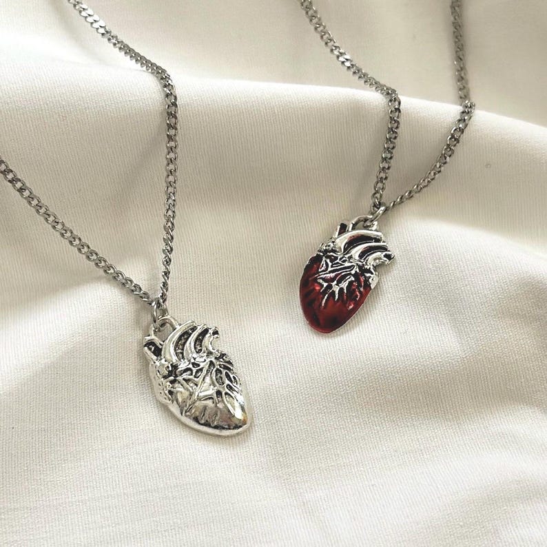 May include: Two silver necklaces with anatomical heart pendants. One heart is silver, the other is red.