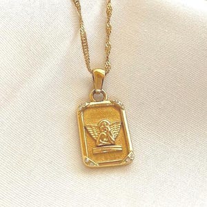 Close-up of 18k gold angel pendant necklace highlighting detailed cherub engraving and polished gold finish