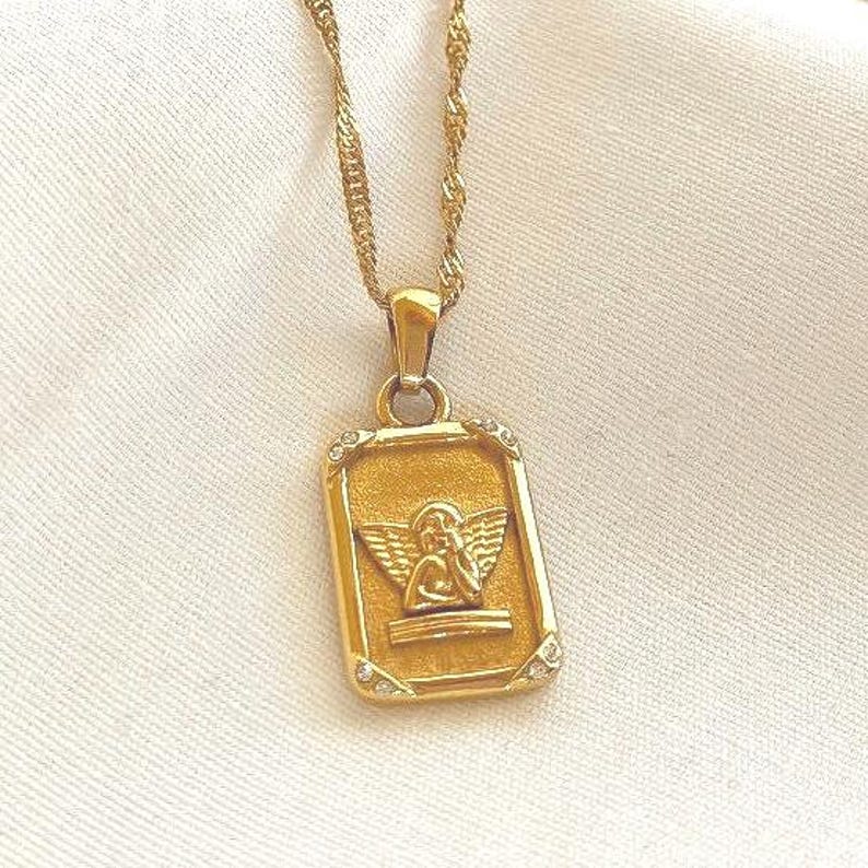 Close-up of 18k gold angel pendant necklace highlighting detailed cherub engraving and polished gold finish